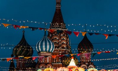 St. Basil's Cathedral and the festival's multicolored flags are suspended overhead along with small, glowing garlands. Fair at the Kremlin. Holiday atmosphere on new year's eve.Closeup, background.