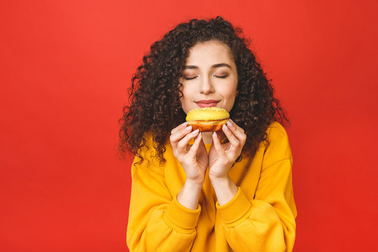 Close Up Portrait Of A Satisfied Pretty Young Girl Eating Donuts Isolated Over Red Background.