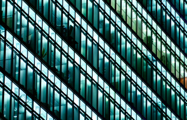 Glass skyscraper with business offices at night. Close up. Rooms in a large corporate building are still lit up as people work late into the night.