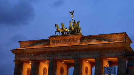 Brandenburg gate with Pariser Platz street sign , Berlin, Germany. The most popular tourist place in Berlin at night, with a beautiful blue sky and clouds, the gate is illuminated with golden light.  © Kost9