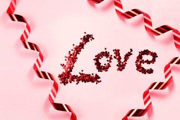 Close up of red gift ribbon in spiral and love word in heart decoration on pink plain background