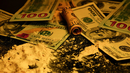 A lot of Illegal drugs scattered on the table and American dollars in a dark room with yellow lighting. Cocaine and dirty money. 