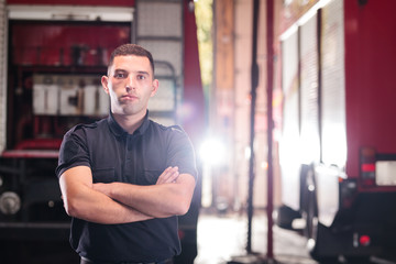Fototapeta na wymiar Professional fireman portrait. Firefighter wearing shirt uniform and fire truck in the background.