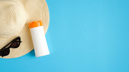 Blank suntan cream bottle, beach hat and sunglasses on blue background. Sun protection on summer vacation concept