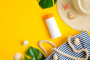 Top view suntan cream bottle, beach bag, female hat and tropical leaves on yellow background. Sun...