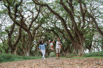 mother and father and two children smile walking through the big trees, enjoying a vacation in the shady garden