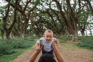 Dad is carrying up his baby while walking in the park while enjoying a vacatio