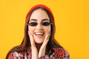 Young woman with stylish sunglasses on color background