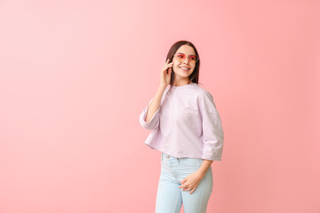 Young woman with stylish sunglasses on color background