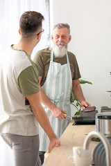 Obraz premium Senior man and his adult son cooking together in kitchen