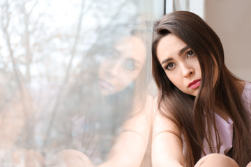 Depressed young woman near window at home