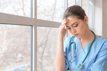 Fototapeta premium Depressed female doctor near window in clinic
