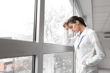 Depressed female doctor near window in clinic