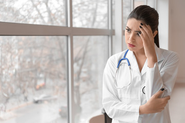 Depressed female doctor near window in clinic