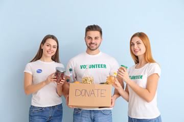 Volunteers with donations for poor people on color background