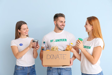 Volunteers with donations for poor people on color background