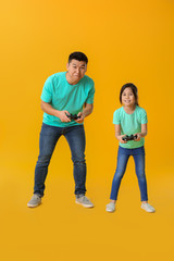 Asian man and his little daughter playing video game on color background