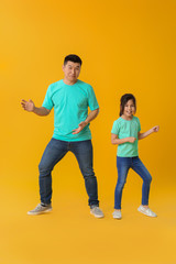 Fototapeta na wymiar Happy Asian man dancing with his little daughter on color background