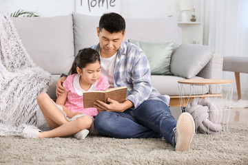 Asian man and his little daughter reading book at home