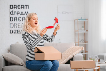 Happy young woman unpacking box with new shoes at home