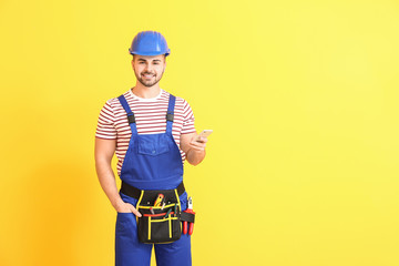 Handsome male worker with mobile phone on color background