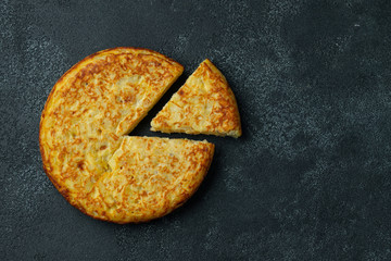 Spanish omelette with potatoes and onion, typical Spanish cuisine on a black concrete background....
