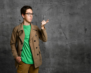 Young teen boy in brown costume and glasses standing and pointing at something with finger over grey concrete wall background