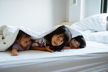 three children play and hide under the covers on the bed when they wake up