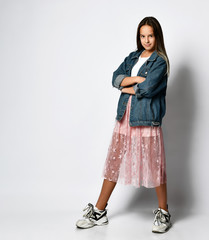 Young smiling teen girl in stylish casual clothes and sneakers standing and looking at camera over white background