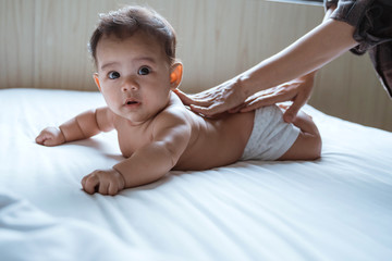 prone baby is rubbed his back by his mother while lying in the bedroom