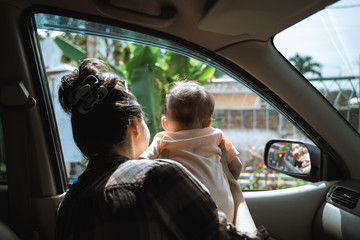 mother holding her little baby to look out the car window when stopped at a tourist spot