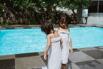 two little girls stand wearing towels after they finish playing in the pool