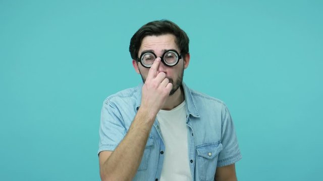 Comical awkward geek adjusting round diopter eyeglasses, looking at camera with stupid funny grimace, having vision problems, eyesight and eye health concept. studio shot isolated on blue background