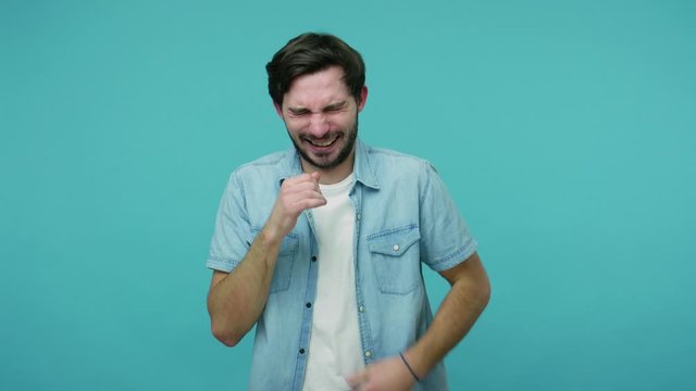 Hilarious crazy laughter. Bearded guy in jeans shirt laughing out loud and wiping tears after hearing anecdote, chuckling giggling being amused by really funny joke. indoor studio shot, isolated