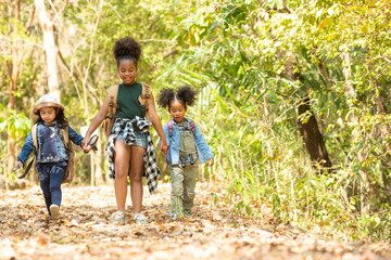 Group of happy pretty little girls holding hands and hiking together with backpacks in forest mountain. Three kids having fun adventure walking in summer day. Children summer leisure activity concept 