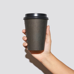 Girl hand hold coffee plastic cup. Grey background with copyspace. Female arm holding paper glass....