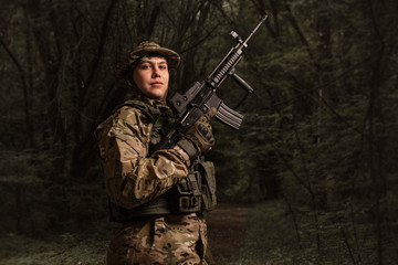 A bottom-up portrait view of a soldier in a military camouflage uniform wearing a  helmet, body armour, and holding a machine gun in a forest.  Sniper. Army.  Border guard.