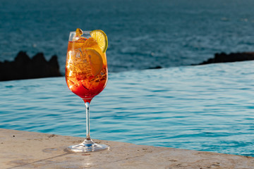 Two cold refreshing red and orange bright colored cocktails with ice cubes and orange slices on pool and ocean background