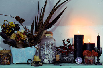 Black candles, feathers and shells in glass jar on the shelf.