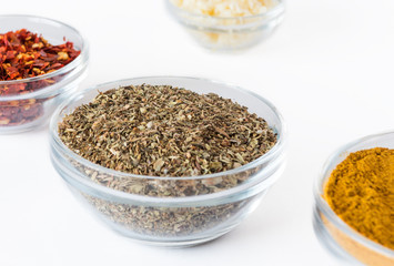 various spices in glass bowls on white background. Culinary Concept with curry, italina herb mix, crushed pepper and garlic
