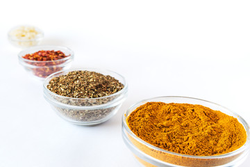 various spices in glass bowls on white background. Culinary Concept with curry, italina herb mix, crushed pepper and garlic