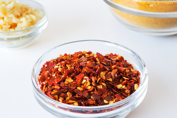 Crushed Pepper spices in glass bowl with blurred curry powder and garlic spices in  background. Culinary Concept