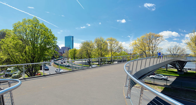 Boston in the spring. Crossing overpass to Charles River esplanade. Tree flowers blooming, city skyline on background, traffic on Storrow Drive.