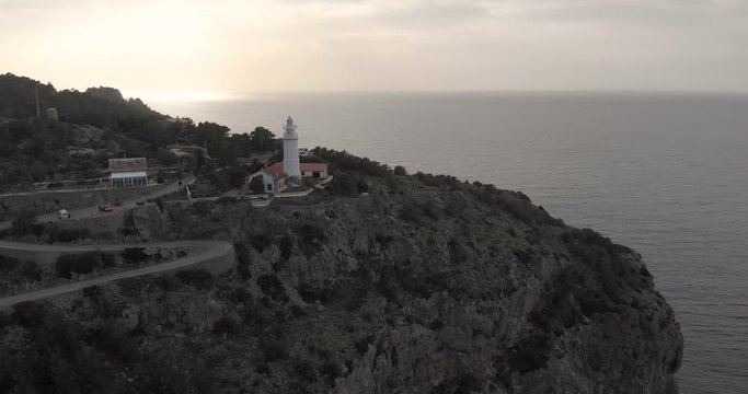 Aerial reverse, drone shot tilting away from the Far des Cap Gros lighthouse, near Soller harbor, at sunset, in Mallorca, Spain 
