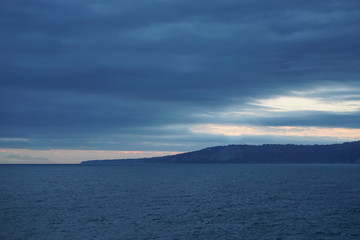 Islands and distant snow-capped mountains viewed from a cruise ship in the Gulf of Alaska, on a misty morning at sea.