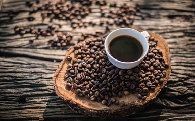 Black coffee in a white cup and spilled coffee beans on the table.