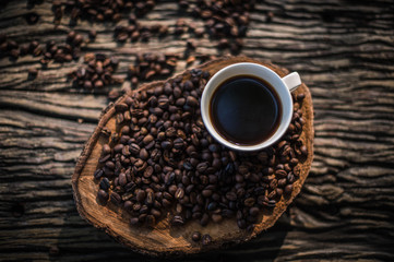 Black coffee in a white cup and spilled coffee beans on the table.