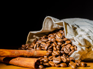 Coffee beans with cinnamon sticks with a coffee bag on a wooden Board on a black background.