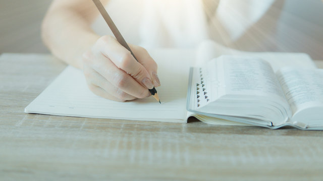 Closeup of bible and woman hand holding a pencil and write something.