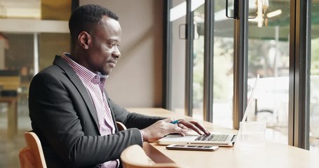  Side view African businessman using laptop in the cafe office by the window getting surprise great good news feel so happy thumb up to the computer screen video meeting online